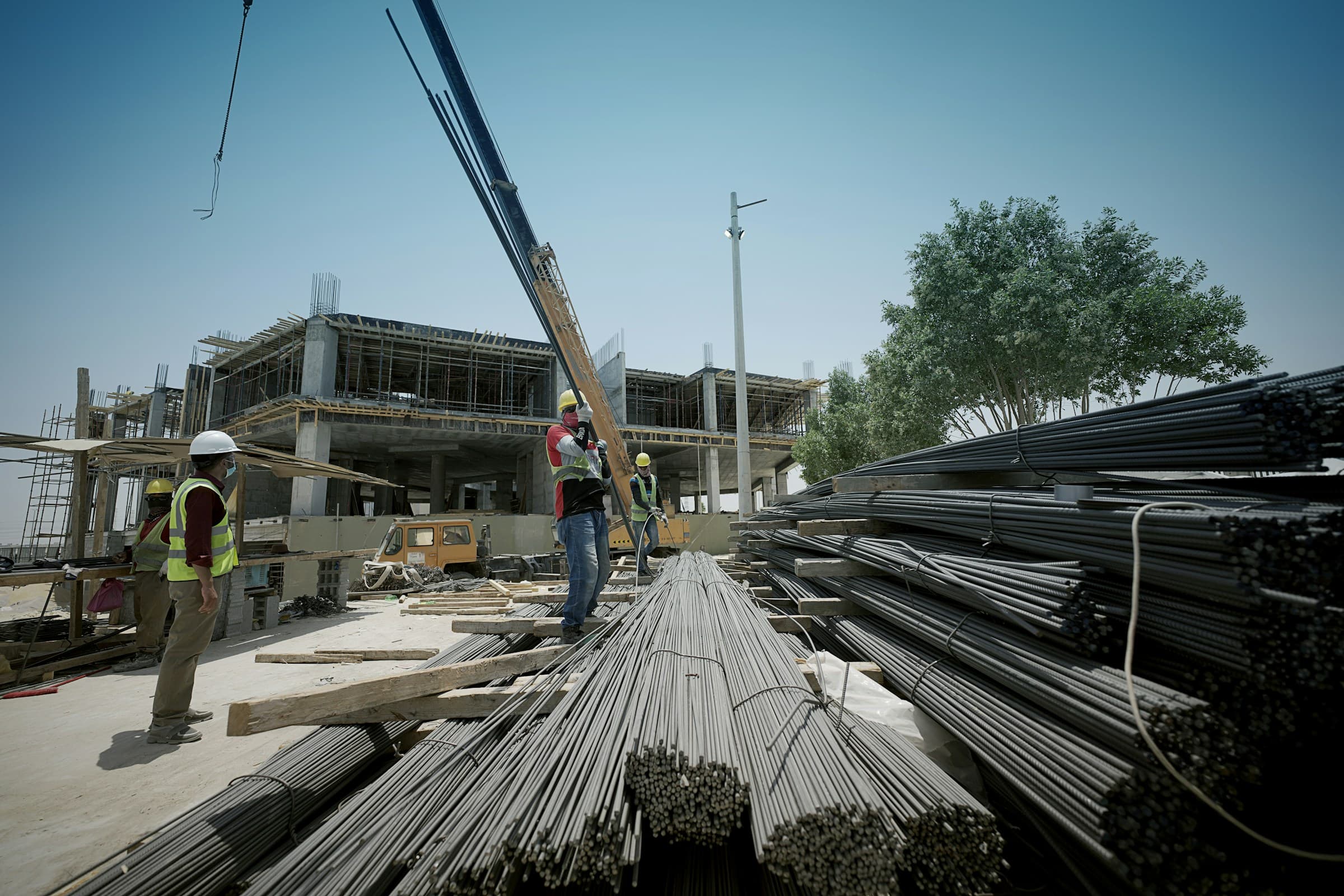 Construction workers and a crane lifting steel reinforcement on an active building site