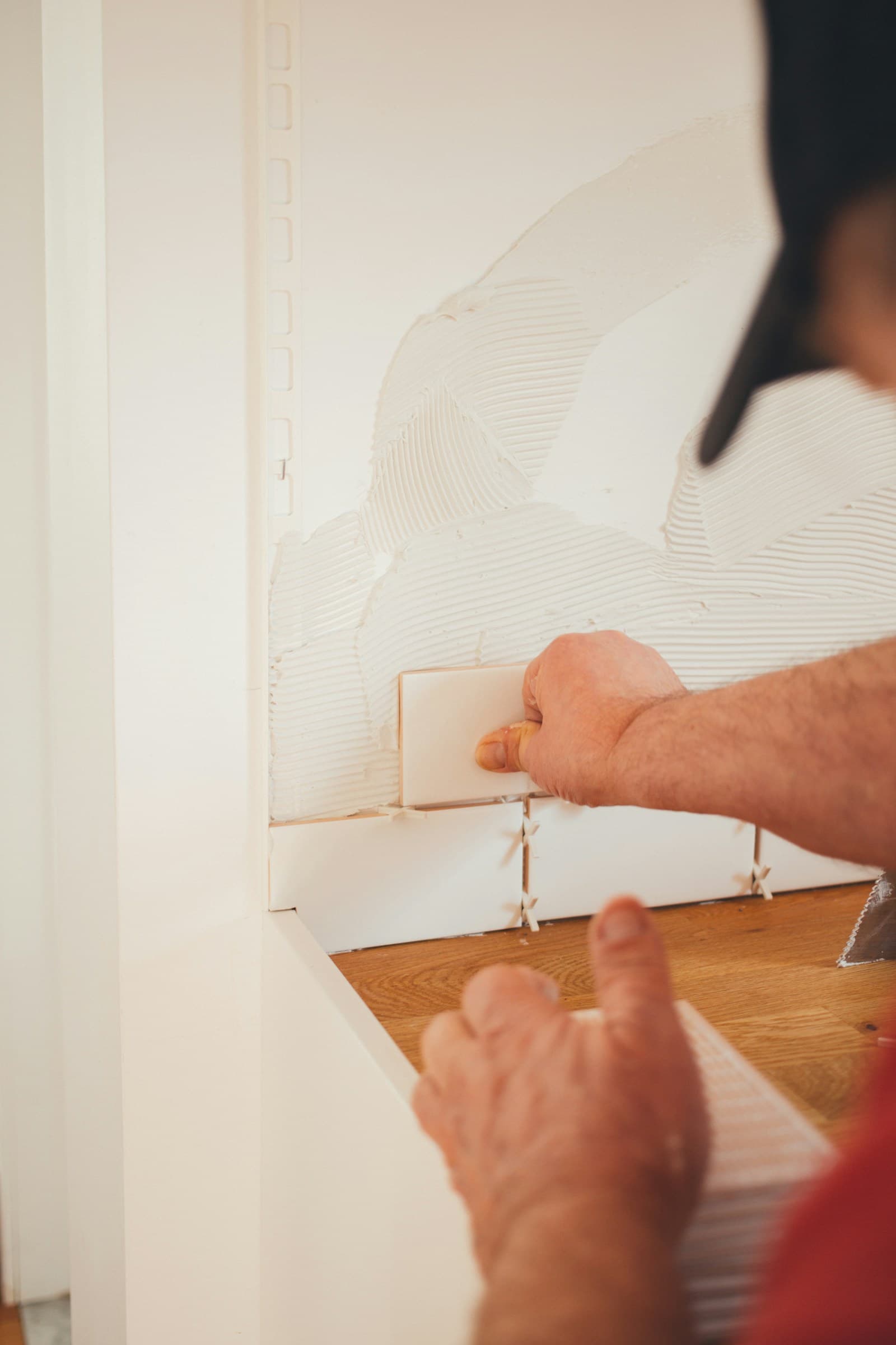 Tiler applying adhesive and setting tiles on a wall